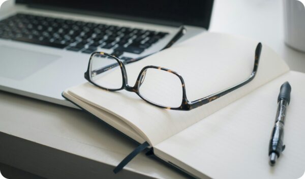 Laptop, pen, and notebook with glasses researching blogging analytics.